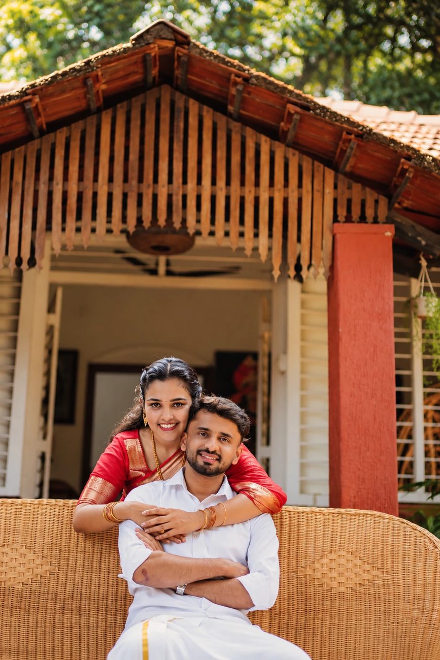 Manisha hugging Pawan from behind on a cane sofa